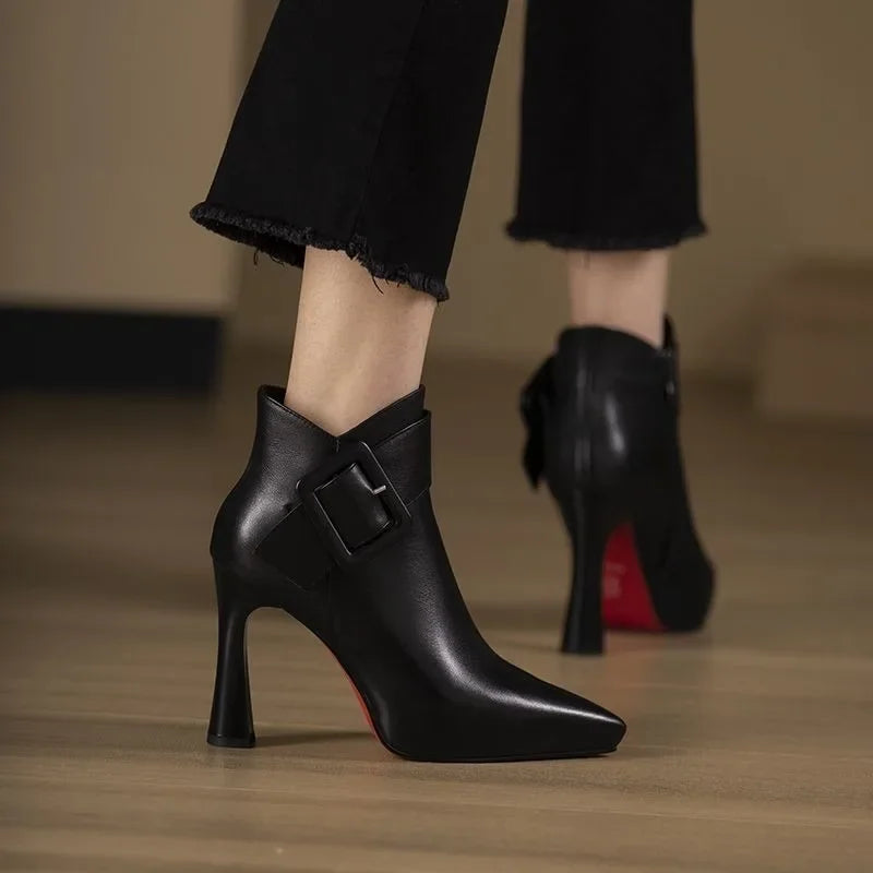 Black high-heeled ankle boots with a buckle detail on a wooden floor.