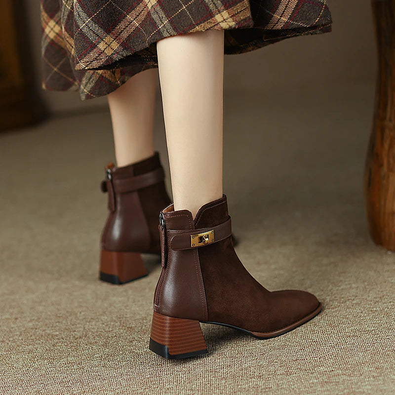 Brown ankle boots with a gold buckle worn by a person on a textured floor.