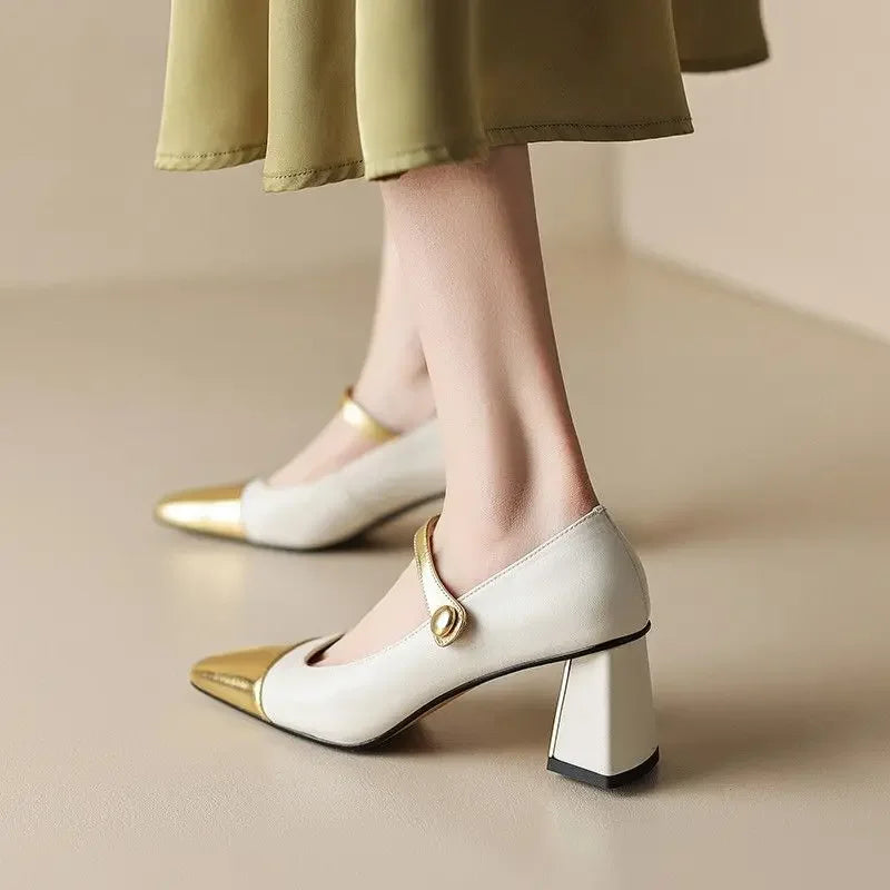 White high-heeled shoes with gold accents worn by a person in a green skirt.