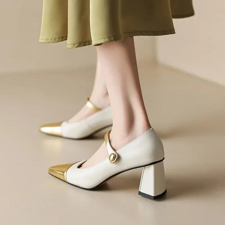 White high-heeled shoes with gold accents worn by a person in a green skirt.