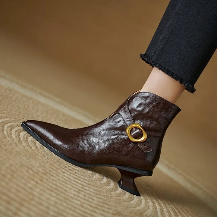 Brown ankle boot with gold buckle on a beige surface