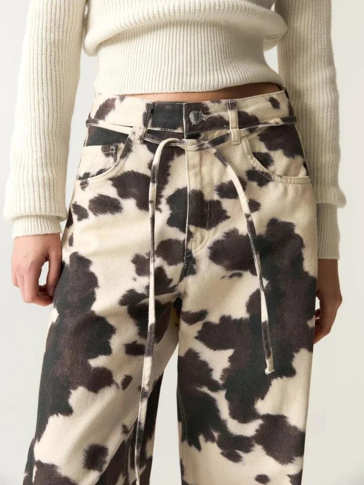 Cow print pants worn with a white sweater on a plain background