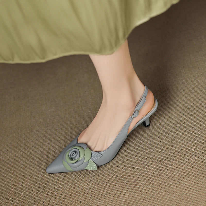 Gray pointed-toe shoes with floral design worn by a person on a brown carpet.