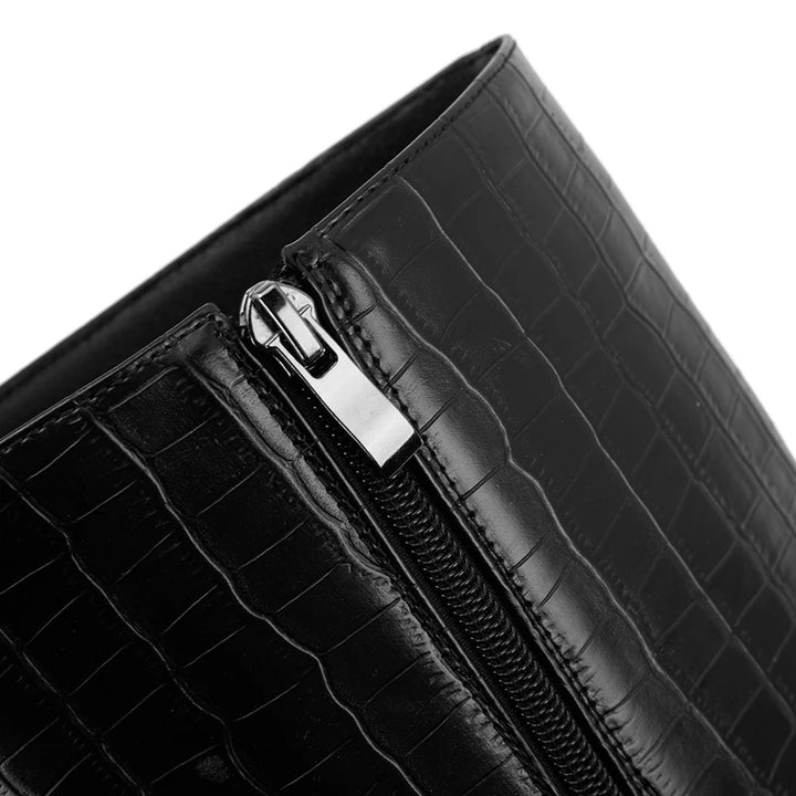 Close-up of a black crocodile-patterned clutch bag with a silver zipper.
