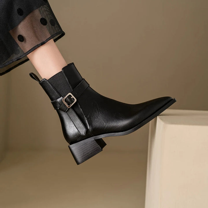 Black ankle boot with a buckle on a neutral background