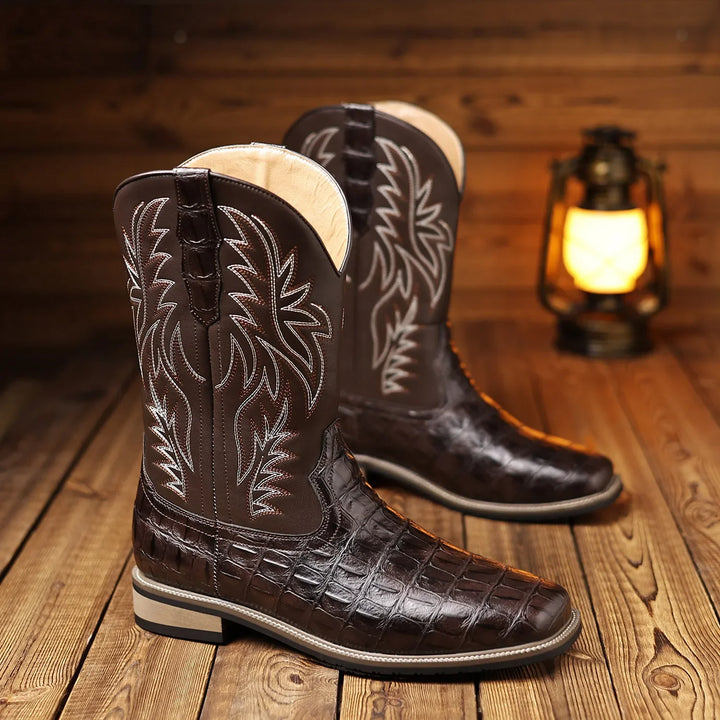 Brown cowboy boots with white stitching on a wooden floor with a lantern in the background