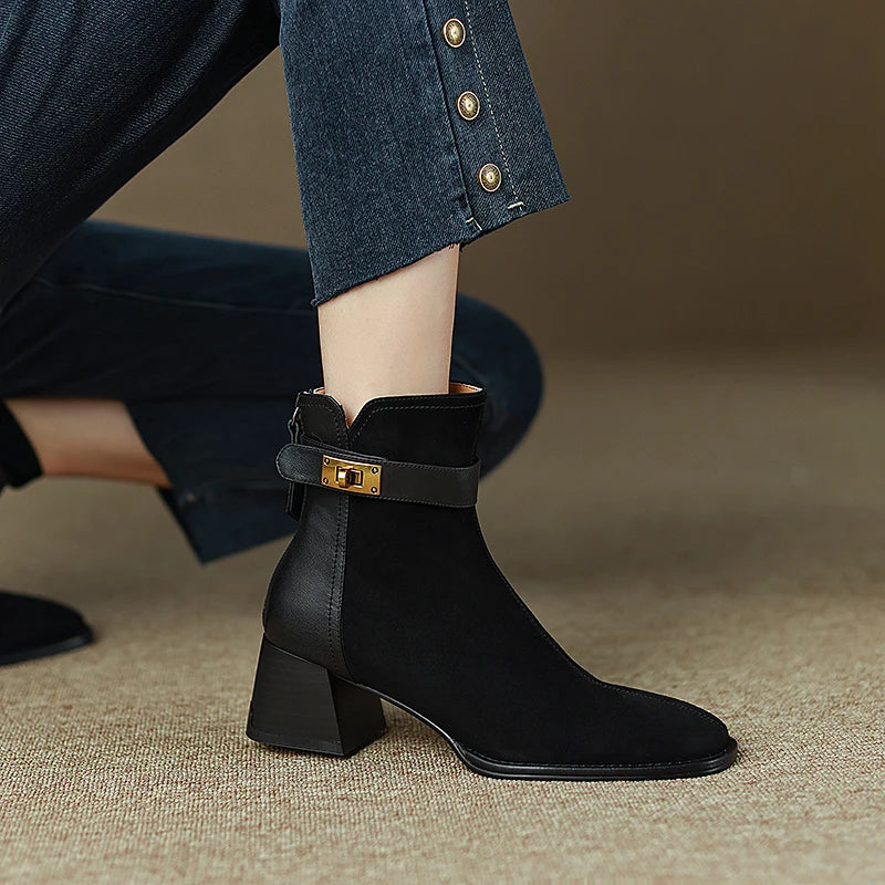Black ankle boot with gold buckle worn by a person in jeans.
