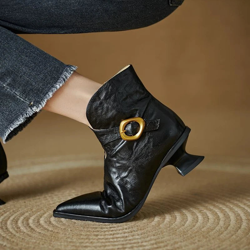 Black ankle boot with gold buckle on a textured brown surface