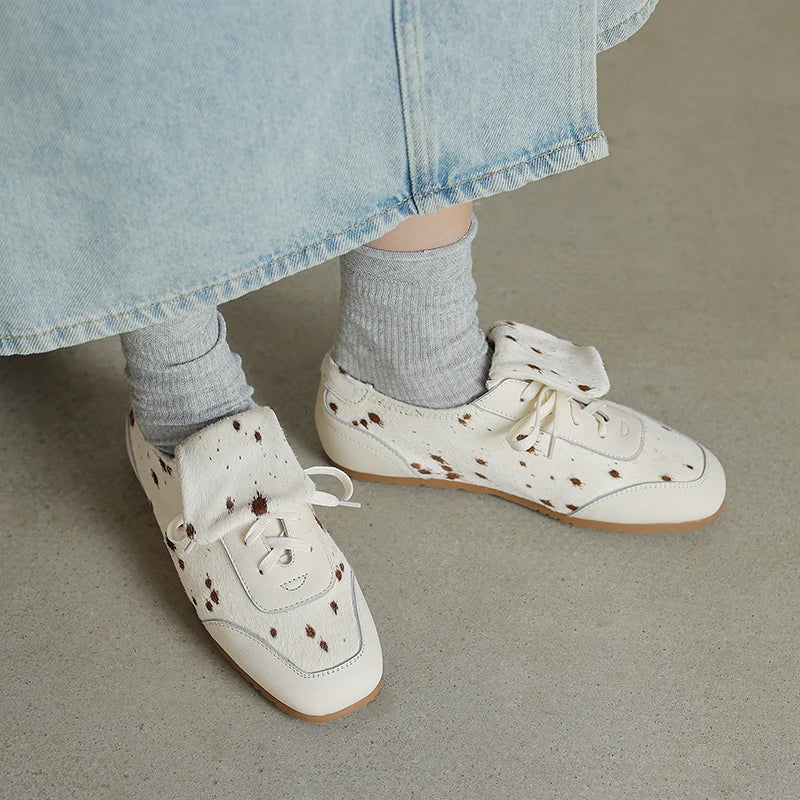 White sneakers with brown speckles worn with light blue denim skirt and gray socks on a neutral background