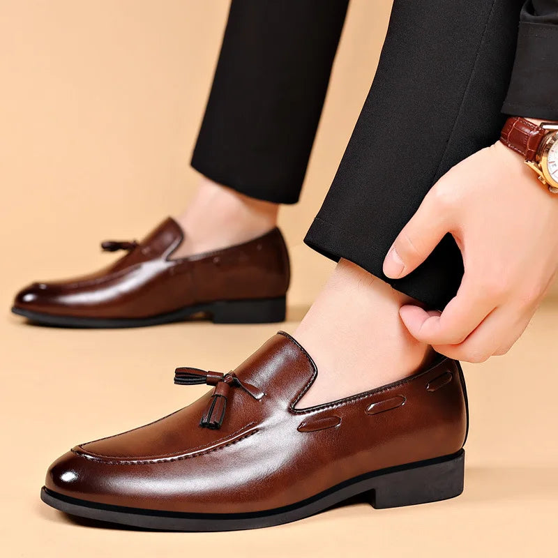 Brown leather loafers with tassels worn by a person on a beige background