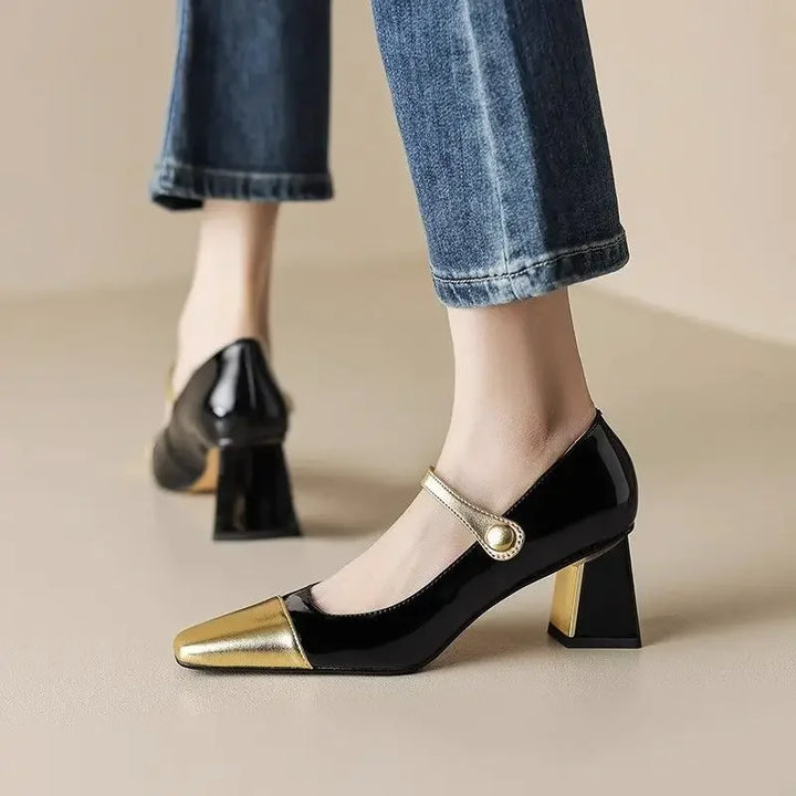 Black and gold shoes worn with rolled-up jeans on a neutral background