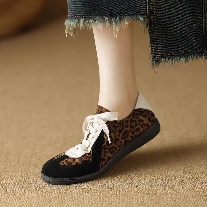 Leopard print sneakers with white laces worn by a person on a beige carpet.