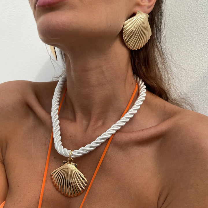 Woman wearing gold shell earrings and necklace against a white background