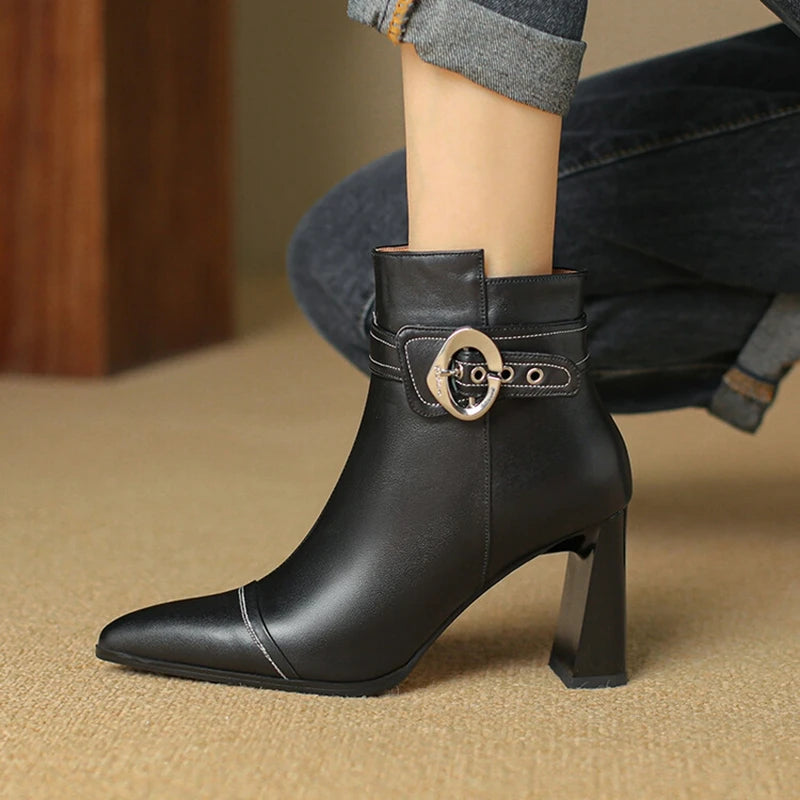 Black leather ankle boot with a gold buckle on a beige carpet