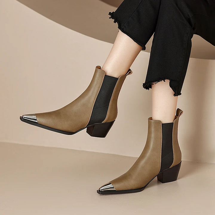 Brown ankle boots with metallic toe tips worn by a person on a beige background