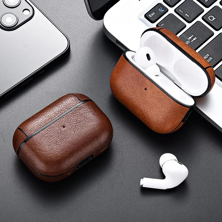 Brown leather cases with white wireless earbuds on a dark surface with a phone and keyboard.