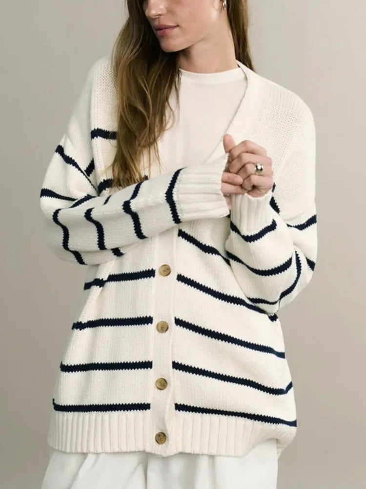 Woman wearing a white cardigan with black stripes on a plain background