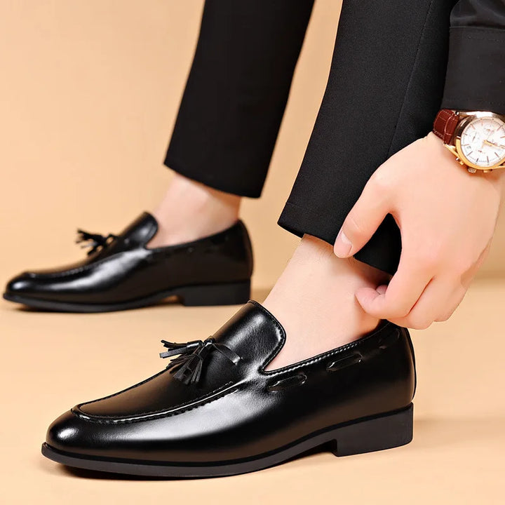 Black leather loafers with tassels worn by a person on a beige background