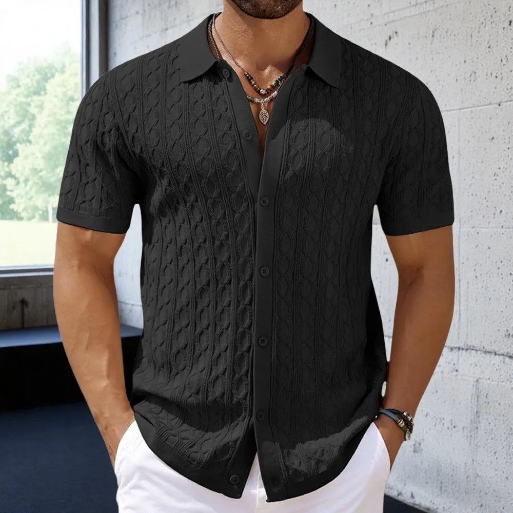 Man wearing a black textured short-sleeve shirt against a concrete wall.