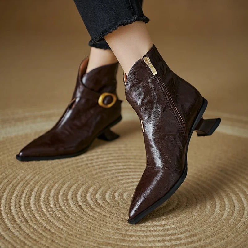 Brown leather ankle boots with a gold buckle on a beige surface