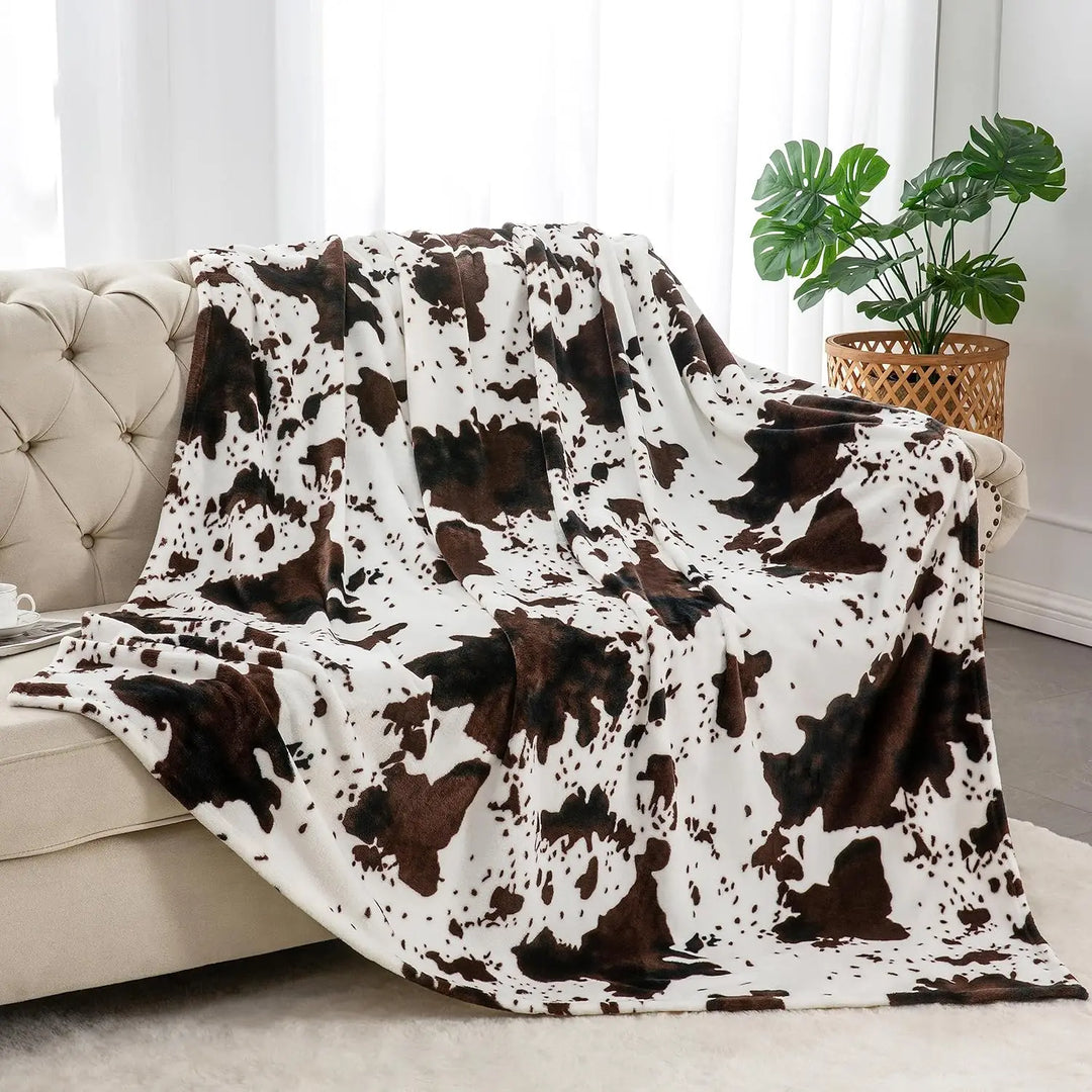 Cow print blanket draped over a sofa in a living room setting with a plant in the background.