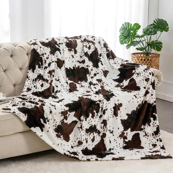 Cow print blanket draped over a sofa in a living room setting with a plant in the background.