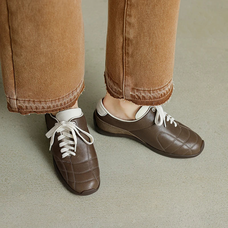 Brown shoes with white laces worn with brown pants on a neutral background