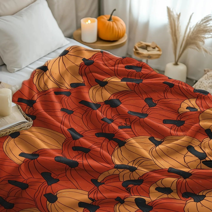 Pumpkin-patterned blanket on a bed with candles and pumpkins in the background