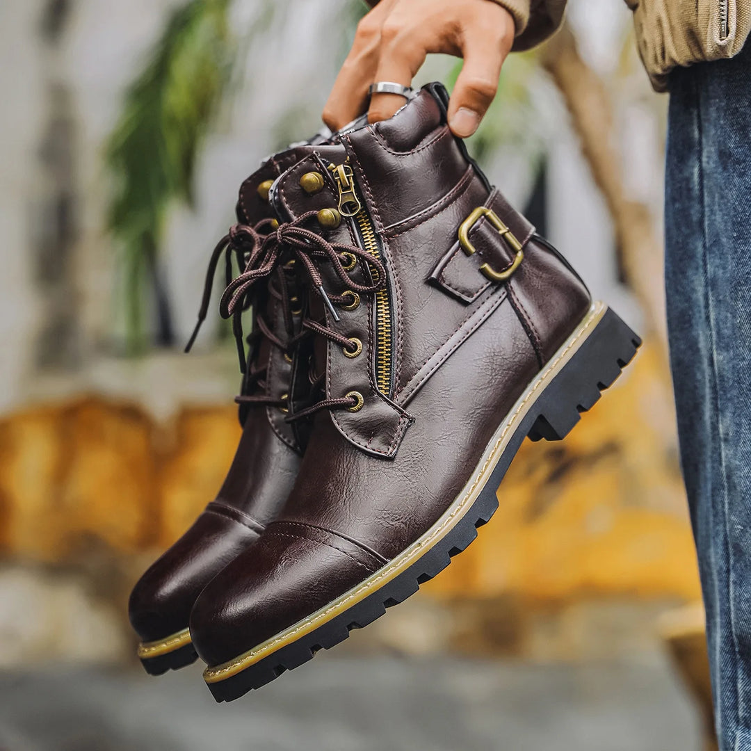 Brown leather boots with gold accents held by a person against a blurred outdoor background