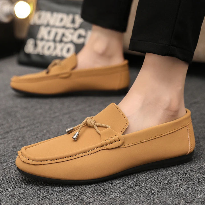 Brown loafers worn on a gray surface with a blurred background