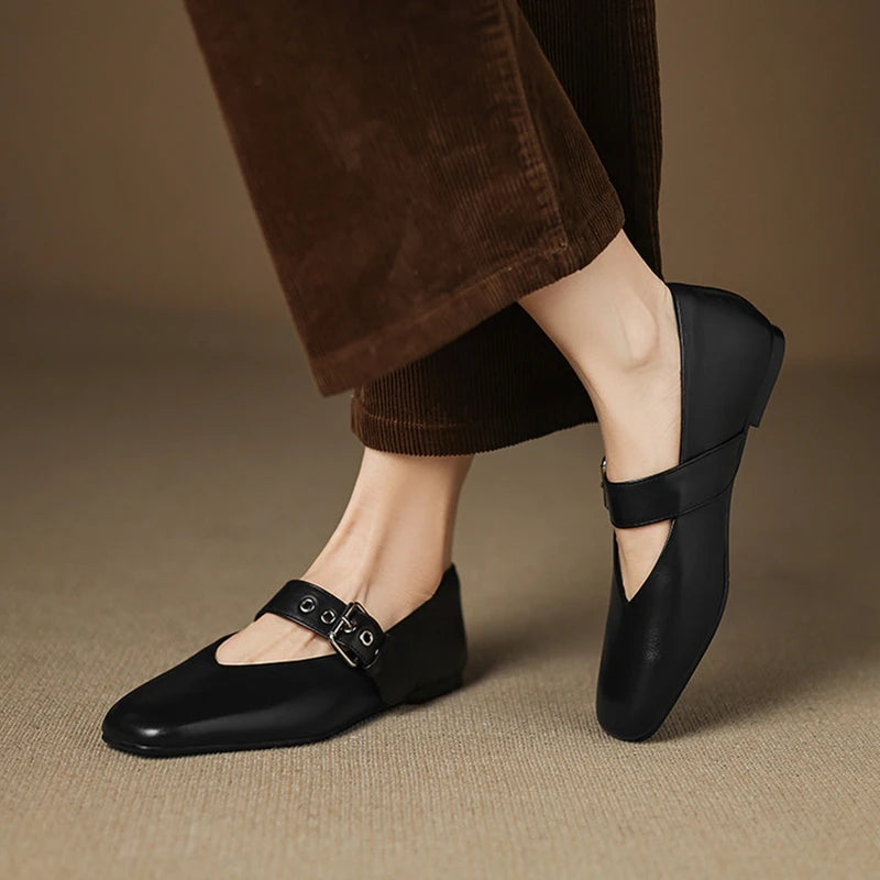 Black shoes with buckles worn by a person on a beige background