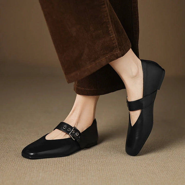 Black shoes with buckles worn by a person on a beige background