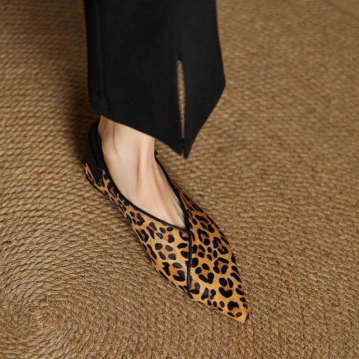 Leopard print shoes worn with black pants on a textured brown surface