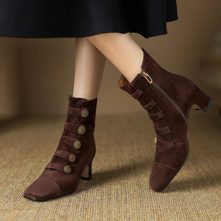 Brown suede high-heeled boots with decorative buttons on a textured surface