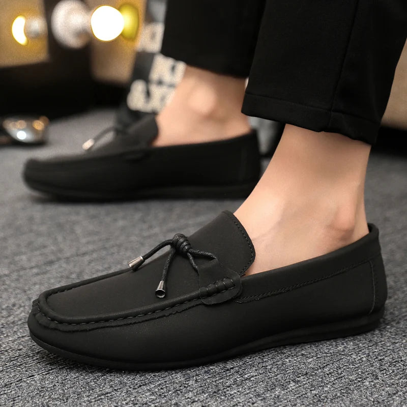 Black loafers worn with black pants on a textured surface.