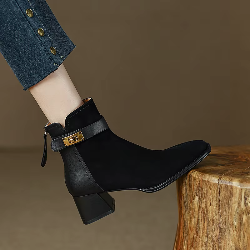 Black ankle boot with a gold buckle on a wooden block against a brown background