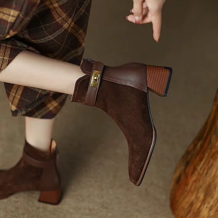 Brown ankle boots with a gold buckle worn by a person, blurred background