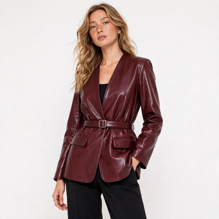 A woman modeling a glossy burgundy leather blazer with a matching belt, worn over a black top and black trousers, against a plain white studio background.