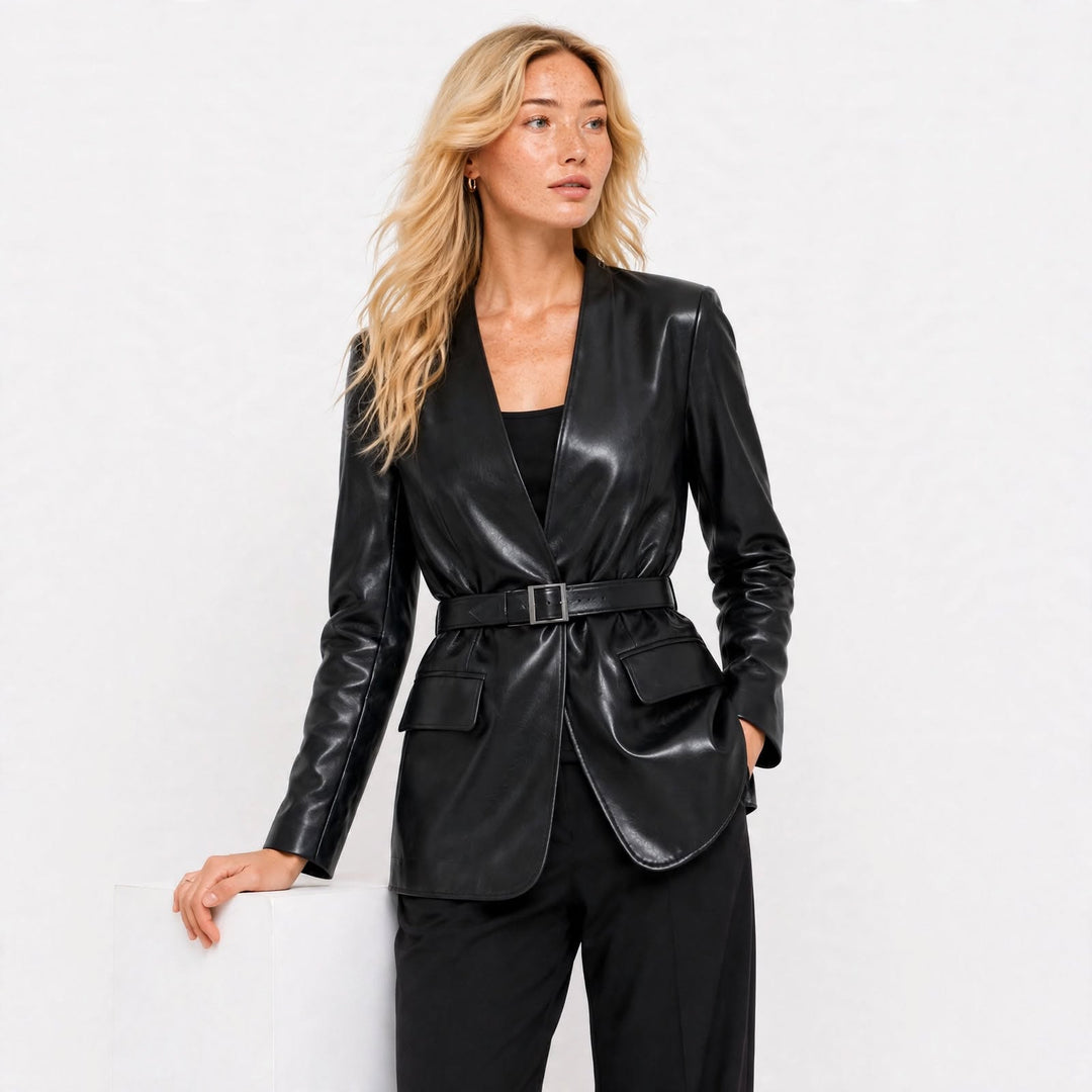 A woman modeling a black leather blazer with a matching belt, styled with black trousers against a plain white studio background.