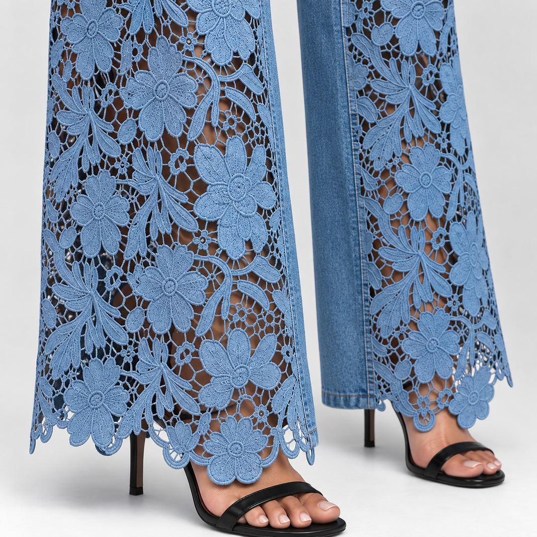 Close-up of a person wearing wide-leg blue jeans with a floral lace overlay and black heeled sandals against a light gray studio background.