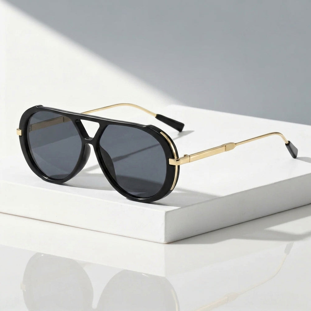 Black aviator sunglasses with gold metal frames and dark gray lenses, resting on a white rectangular block against a light gray background.