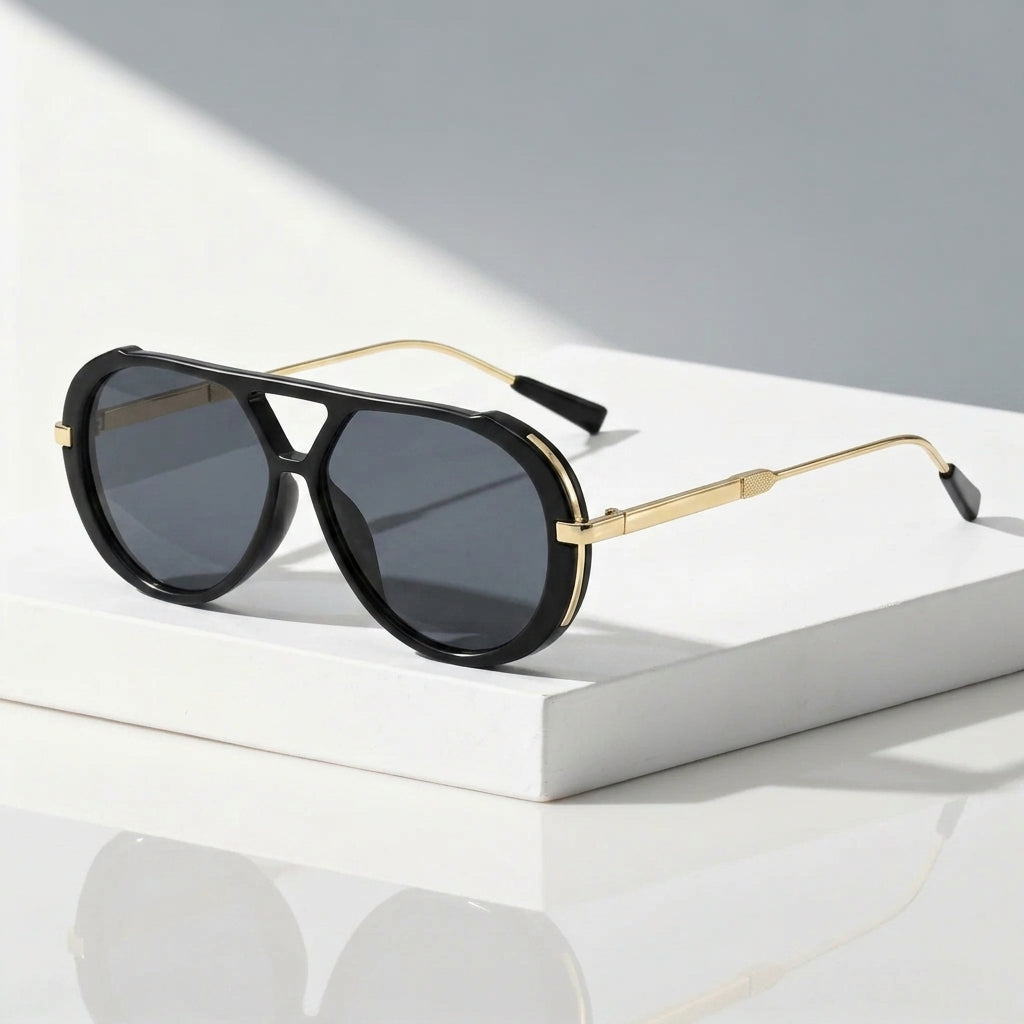 Black aviator sunglasses with gold metal frames and dark gray lenses, resting on a white rectangular block against a light gray background.