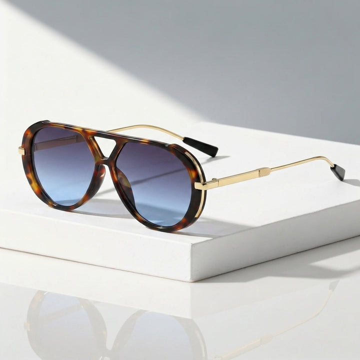 A pair of aviator-style sunglasses with tortoiseshell frames and gold metal arms, resting on a white rectangular block against a light gray background with soft shadows.