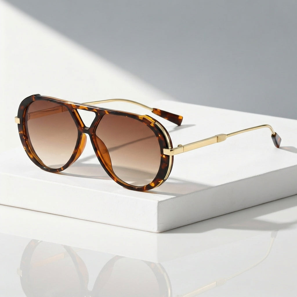 Aviator-style sunglasses with a tortoiseshell acetate frame, brown gradient lenses, and slim gold metal temples, displayed on a white rectangular pedestal against a light gray background.