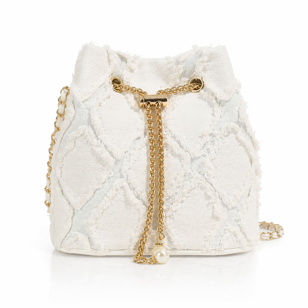 An off-white textured bucket bag with a gold-tone chain strap and a dangling pearl accent, set against a plain white background.